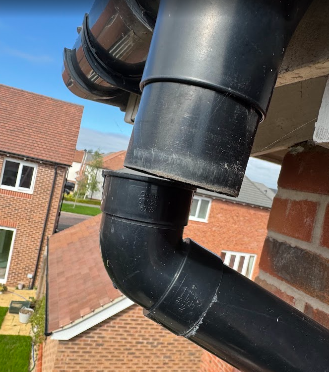 Close-up of a black downpipe and elbow on a brick home.