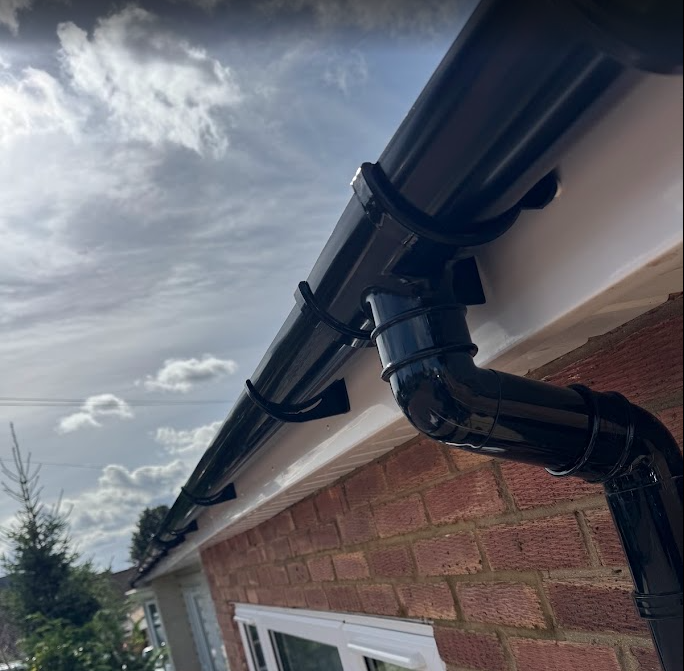 Close-up of black guttering and a downpipe installed on a brick home.